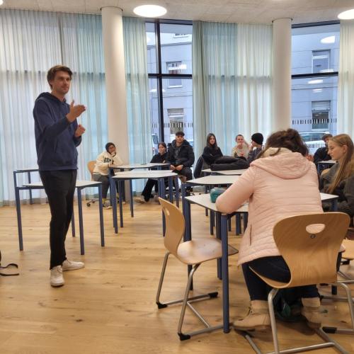 Mann vor Schülern, die an Tischen in der Bibliothek sitzen
