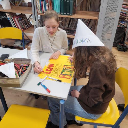 Zwei Jugendliche am Tisch, eine mit Papierhut.
