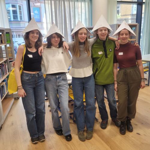Fünf Schüler:innen mit Papierhüten in den Räumlichkeiten der Schulbibliothek