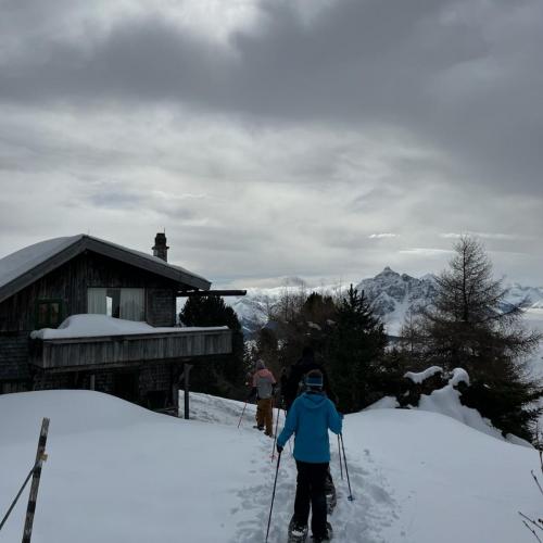 Hütte im Schnee mit Schneeschuhwanderern, die rechts vorbeigehen