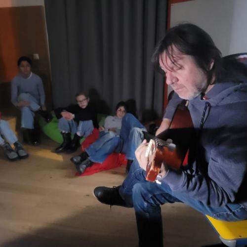 Lehrer spielt Gitarre, Schüler:innen hören zu