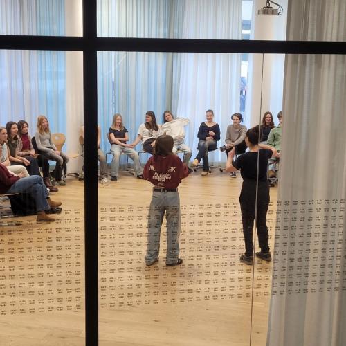 Kinder sitzen im Kreis in der Bibliothek, zwei spielen Theater