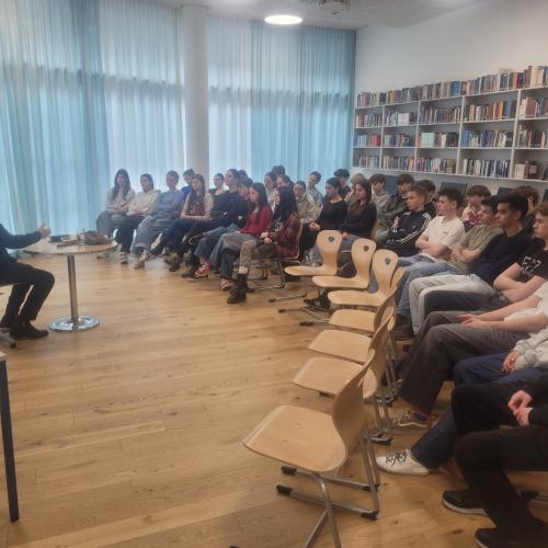 Schüler:innen sitzen im Halbkreis und hören C. W. Bauer zu