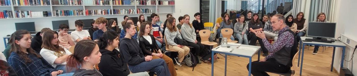 Schüler:innen hören in der Bibliothek Thomas Lackner beim Lesen zu