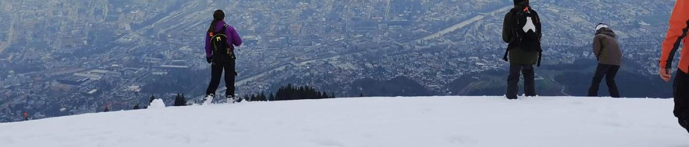 Schüler:innen blicken von einem schneebedeckten Berg auf die Stadt Innsbruck im Tal
