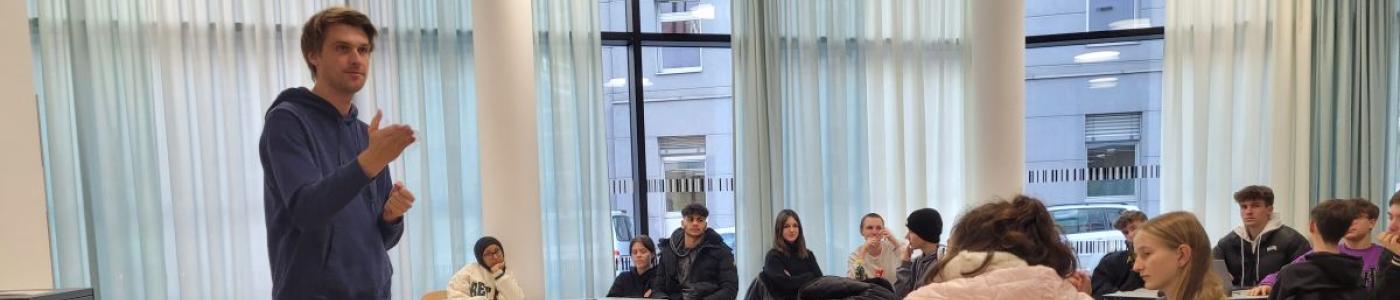 Mann vor Schülern, die an Tischen in der Bibliothek sitzen