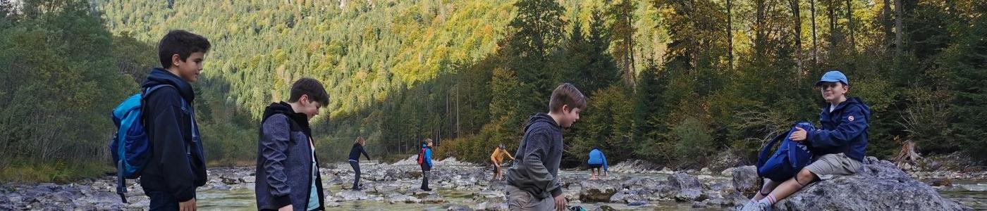 Vier Kinder vor springen über Steine an einem Gebirgssee