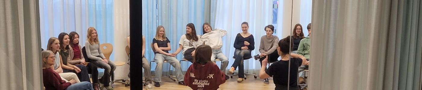 Kinder sitzen im Kreis in der Bibliothek, zwei spielen Theater