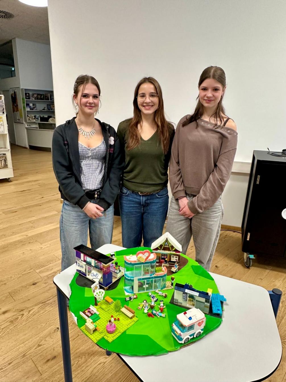 Drei Schülerinnen präsentieren eine LEGO-Landschaft 