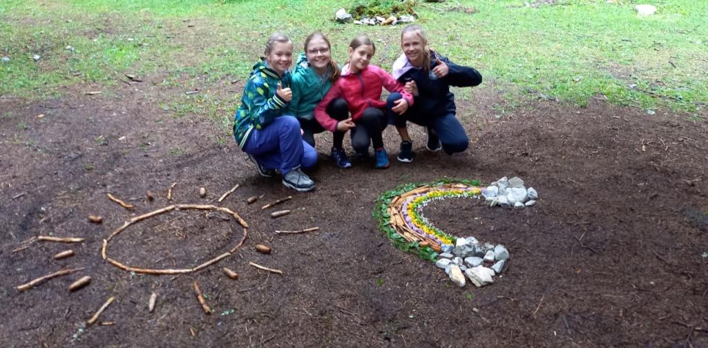 Vier Kinder hocken hinter Figuren aus Stöcken am Waldboden