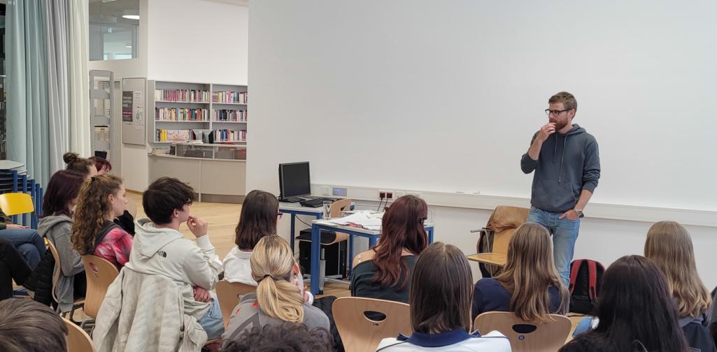 Ein Mann spricht vor Schülern, die im Kreis um ihn herumsitzen