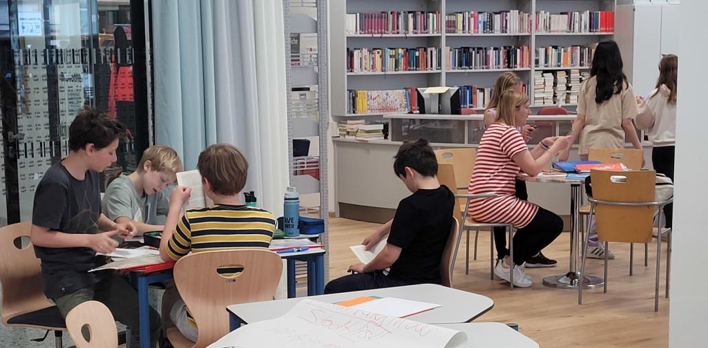 Schüler:innen arbeiten an Tischen, Bücherregale im Hintergrund